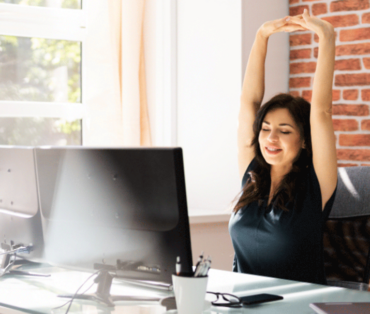 Woman stretching at desk behind computer