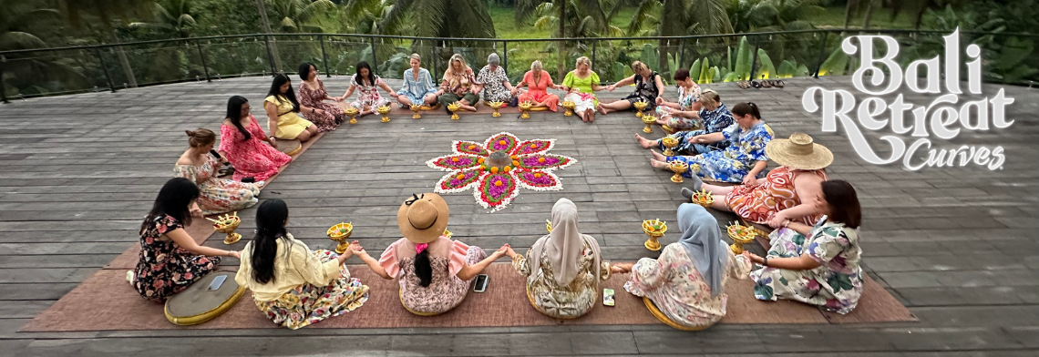 A diverse group of women holding hands in a large, supportive circle around a vibrant flower mandala ceremony during the Curves Bali Retreat at Soulshine Ubud.